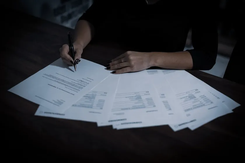 Pessoa revisando documentos da declaração do Imposto de Renda espalhados sobre a mesa